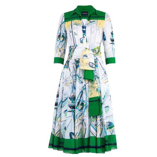 A white midi dress with an all-over abstract blue and yellow nautical print. The dress features a green-trimmed shirt collar, 3/4 sleeves with green cuffs, a button-front, a pleated A-line skirt with a green hem, and a matching fabric sash with a green end.